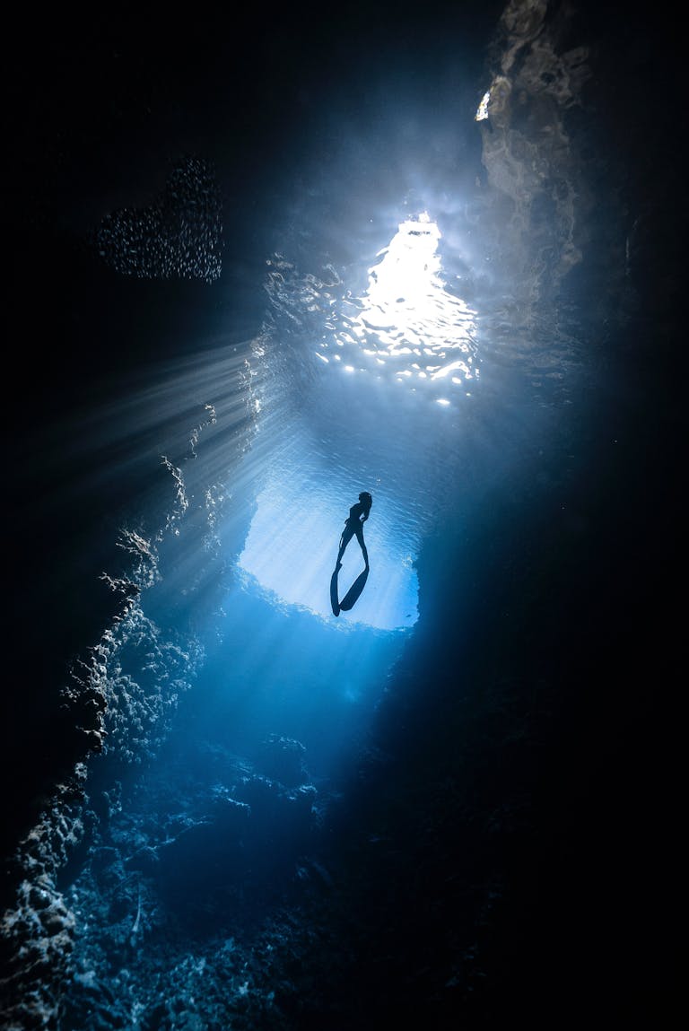 A breathtaking view of a scuba diver silhouetted in a sunlit underwater cavern.