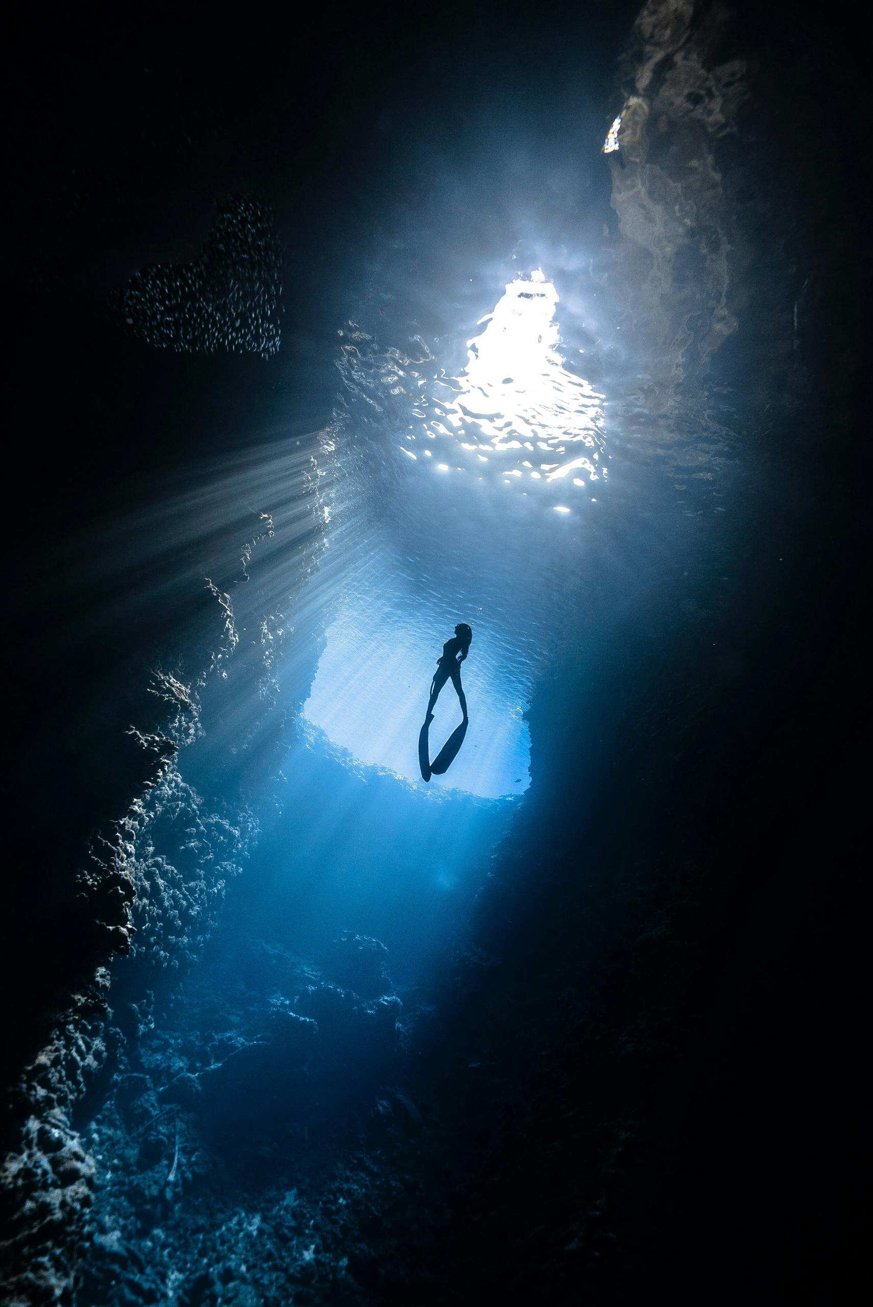 A breathtaking view of a scuba diver silhouetted in a sunlit underwater cavern.