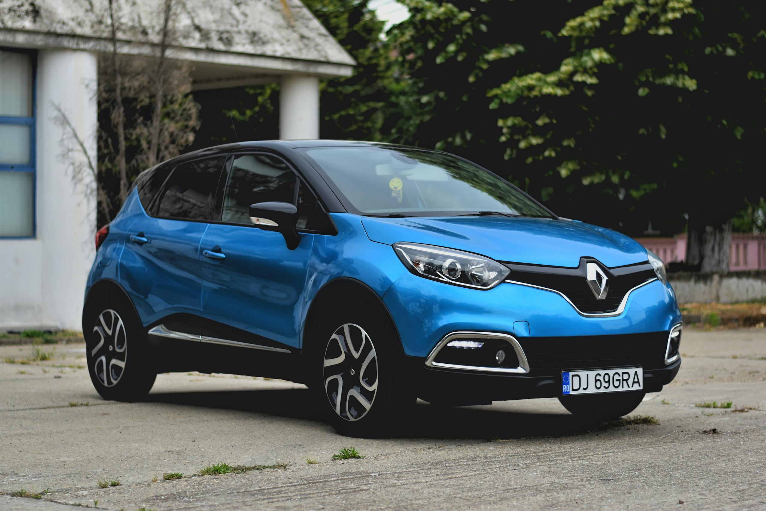 A vibrant blue Renault Captur parked outdoors with trees in the background.