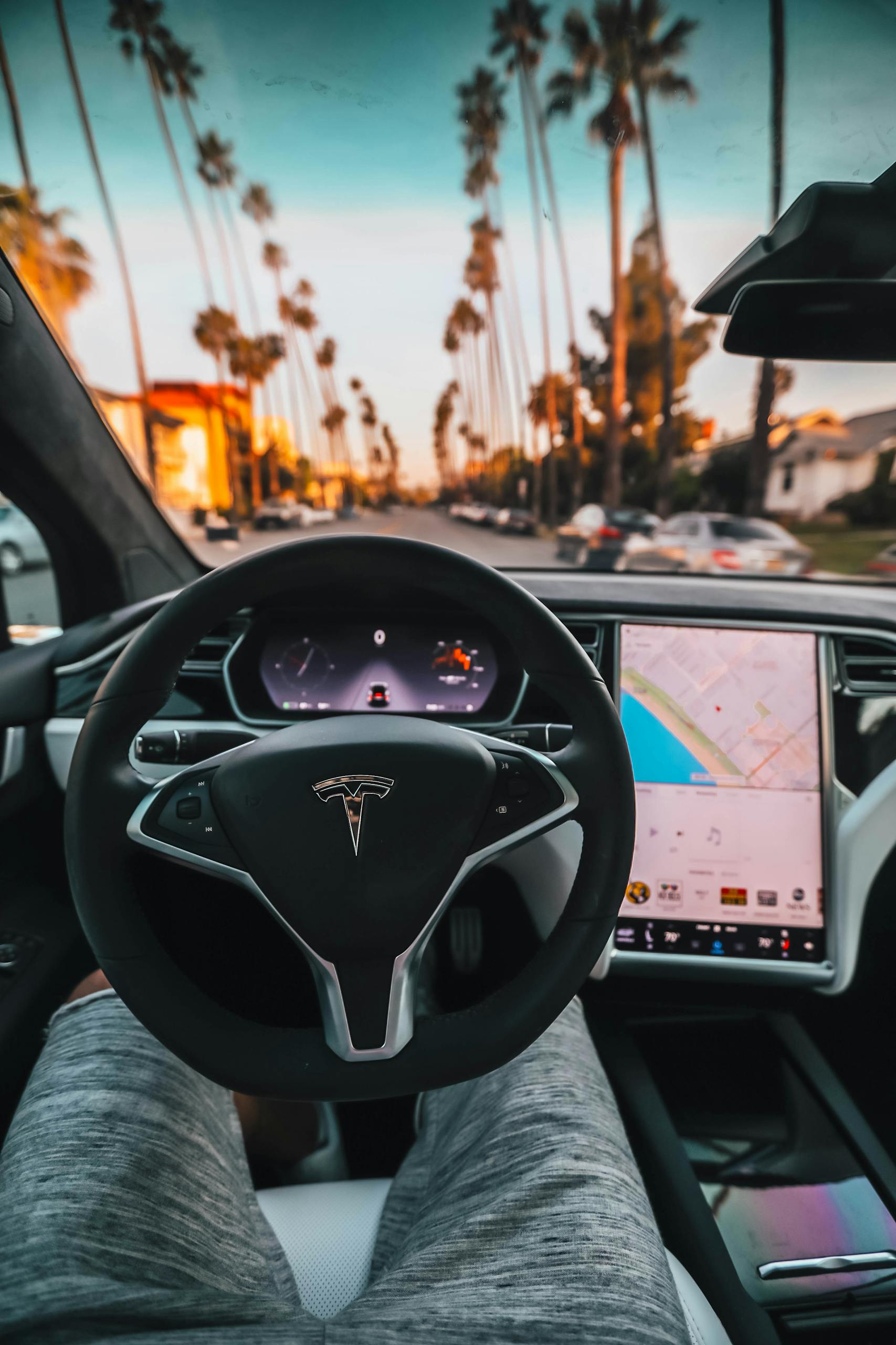 Interior view of a Tesla Model X steering through palm-lined streets of Santa Monica at twilight.